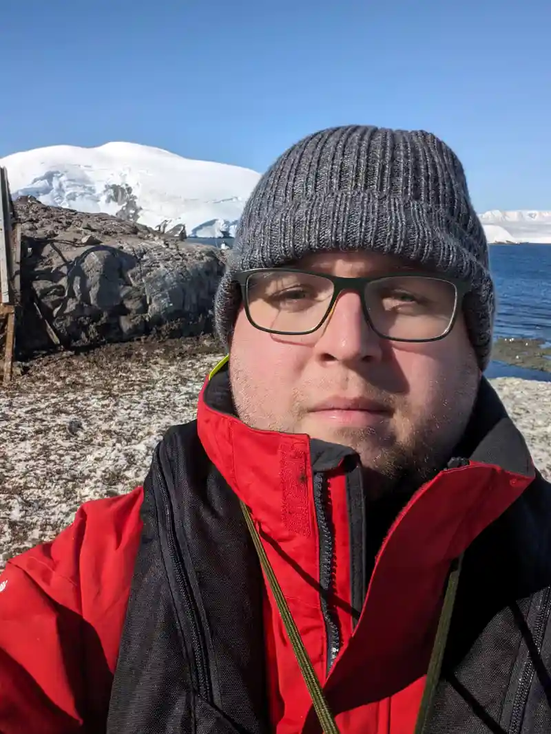 Portrait of Alex Lebens in a red jacket and grey winter cap.